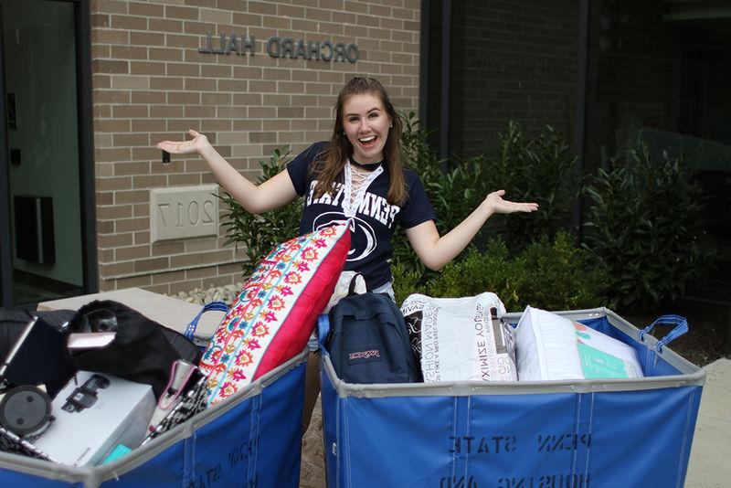 female student standing in front of Orchard Hall with bins to move in